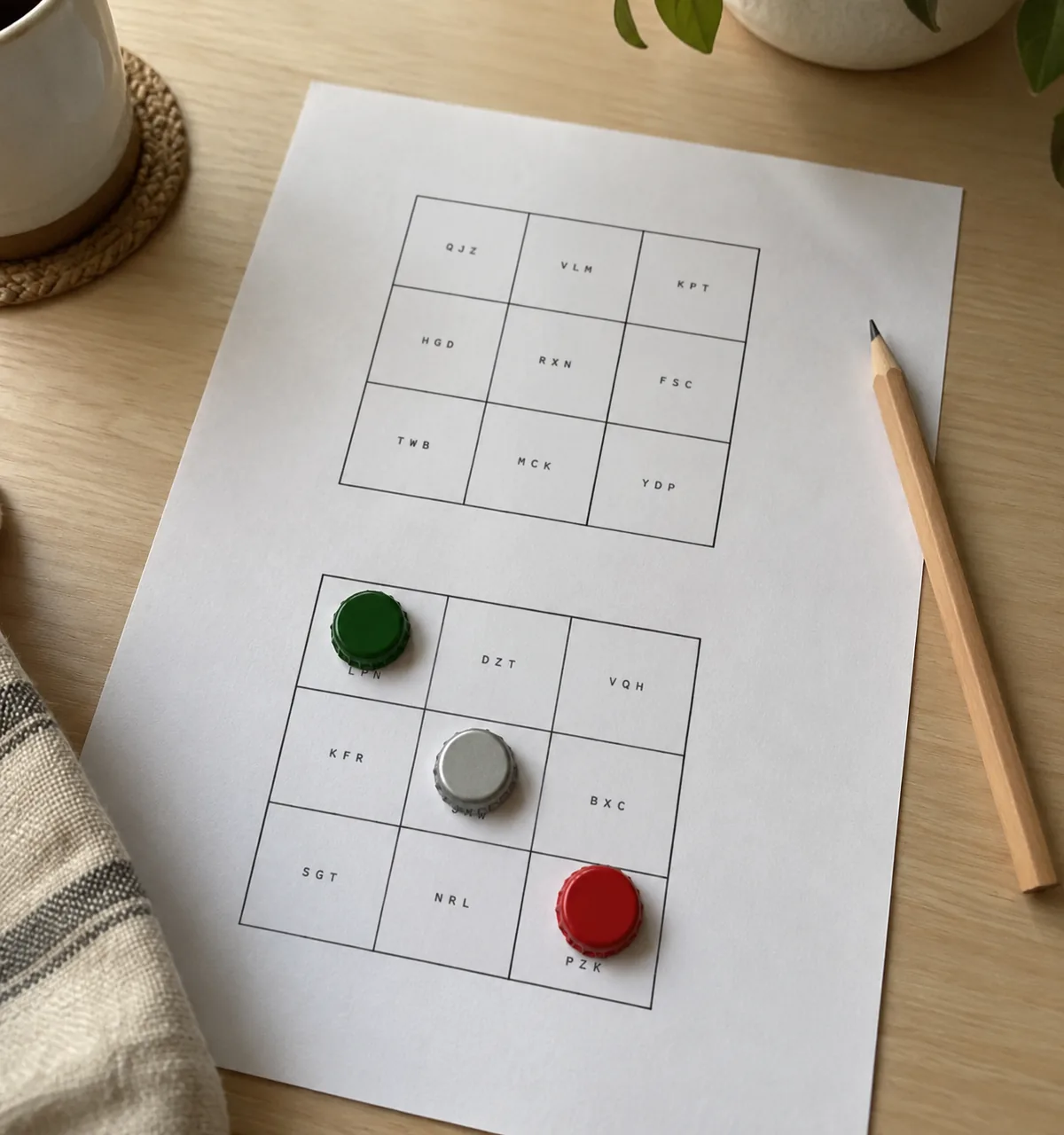 Folha A4 com duas cartelas de bingo 3×3 em preto e branco, três tampinhas marcando casas de uma cartela, e um lápis ao lado. Imagem ilustrativa