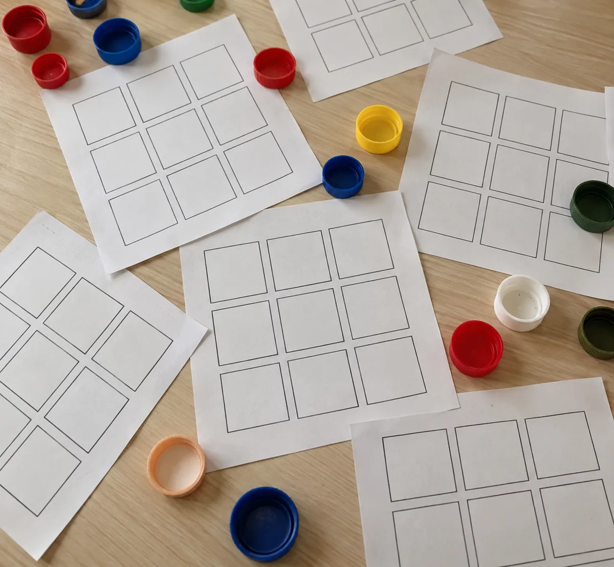 Cartelas de bingo em branco espalhadas e misturadas com tampinhas coloridas sobre a carteira. Imagem ilustrativa